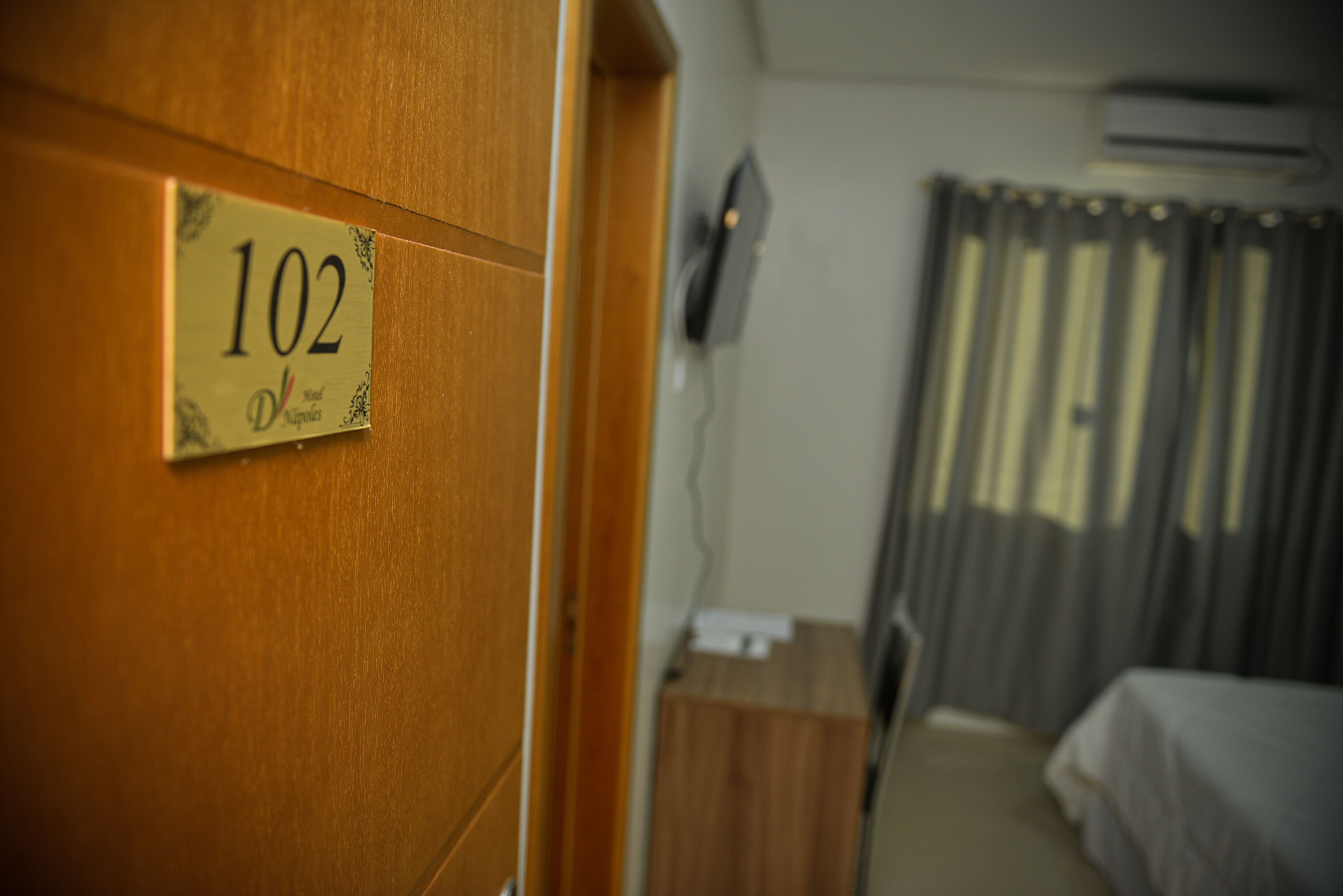 Et hotelværelse med en dør af træ med teksten '102' og en seng med hvidt sengetæppe.