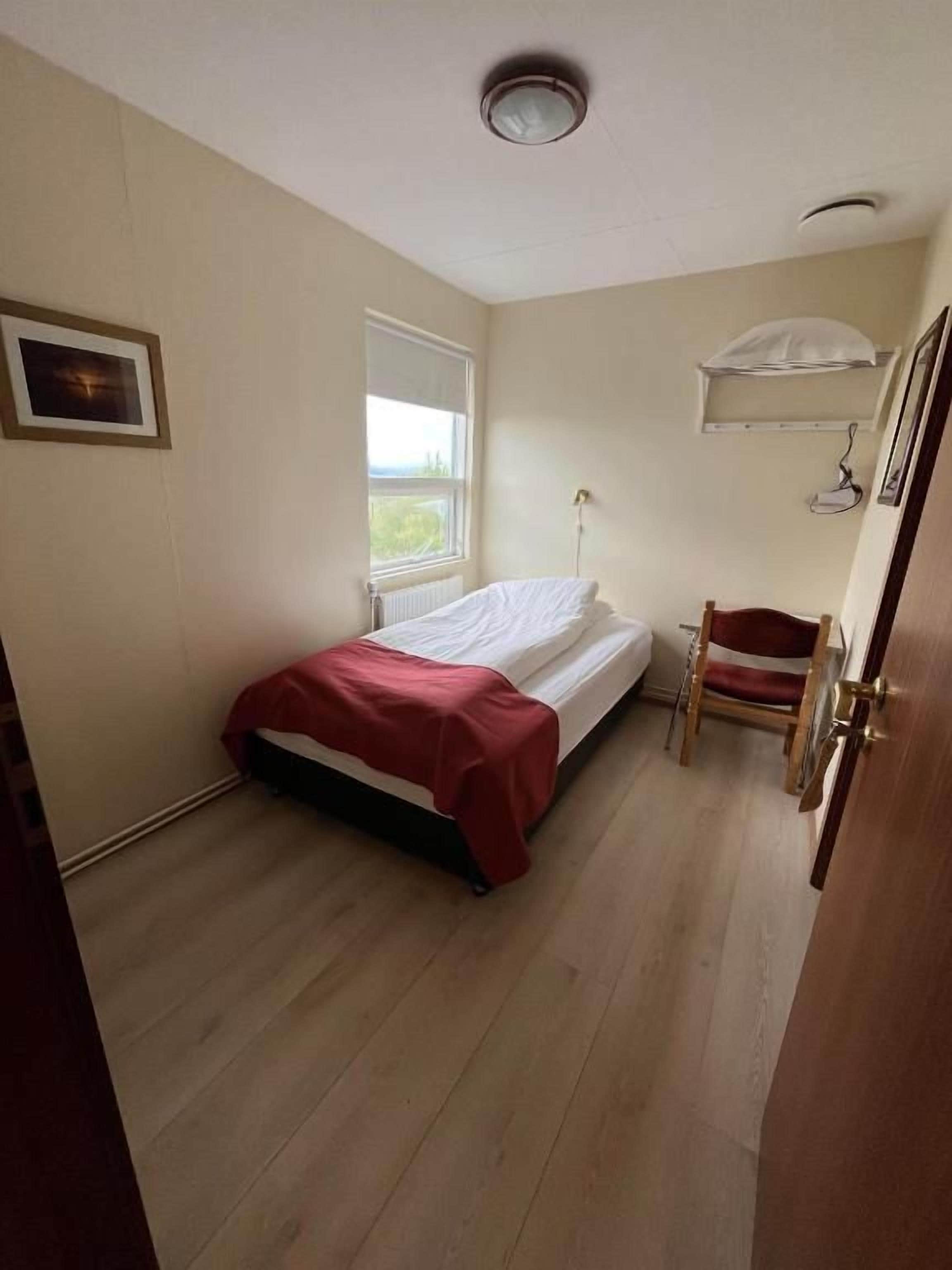 Una habitación pequeña con una cama, una silla, un ventanal y un radiador.
