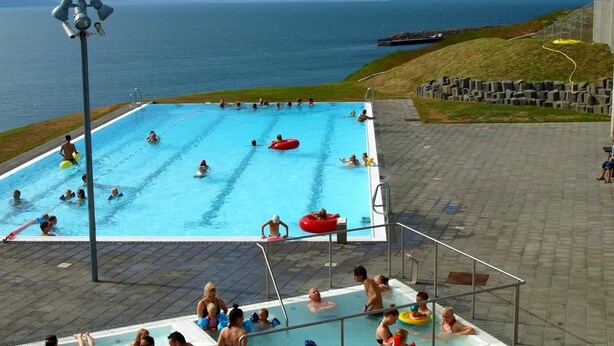 A swimming pool with people, including children and adults, swimming and playing. - Sunnuberg Guesthouse (Skagafjörour)