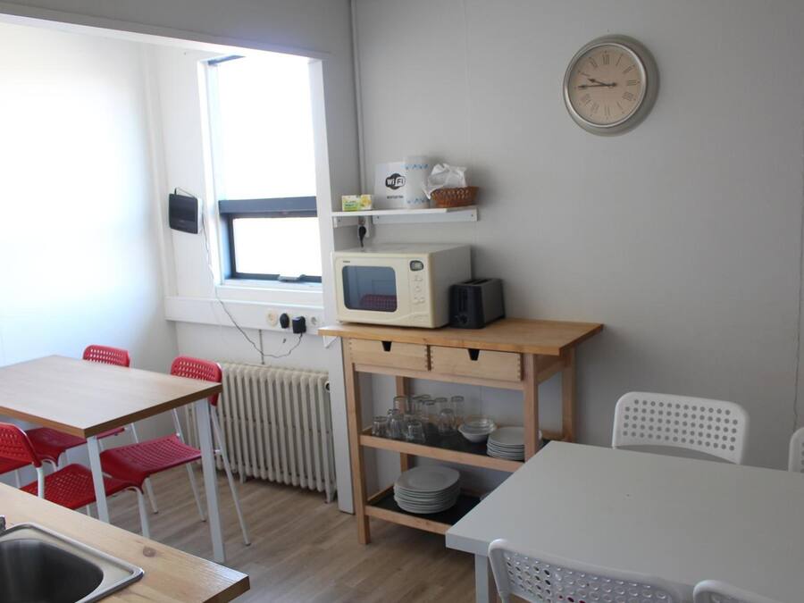 A small kitchenette with a microwave, a sink, and a window. There are red chairs and a white table.