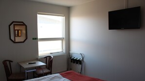 A hotel room with a bed, a desk, a chair, a TV, and a window. - Sunnuberg Guesthouse (Skagafjörour)