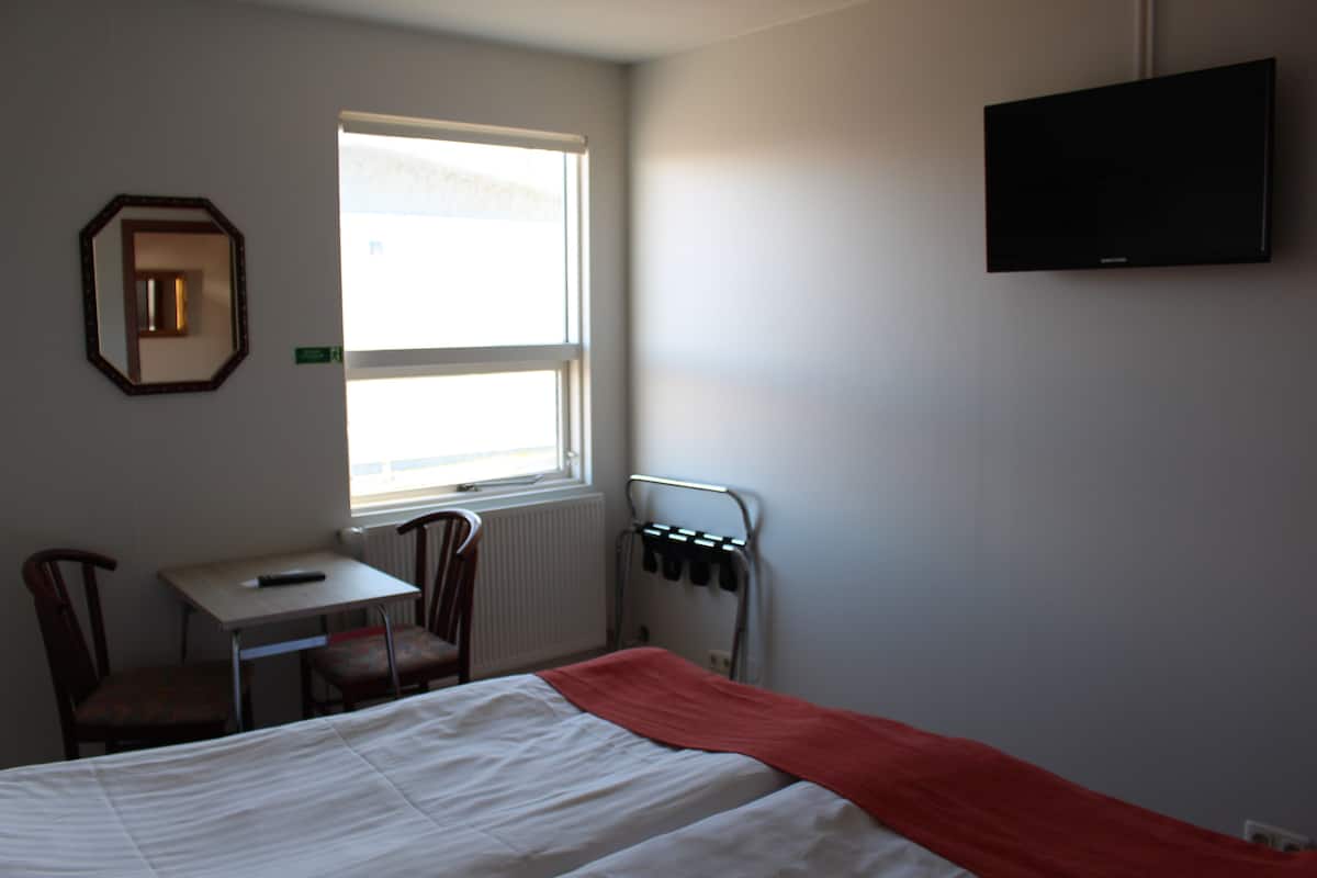 Una habitación de hotel con cama, escritorio, silla, televisión y ventana.
