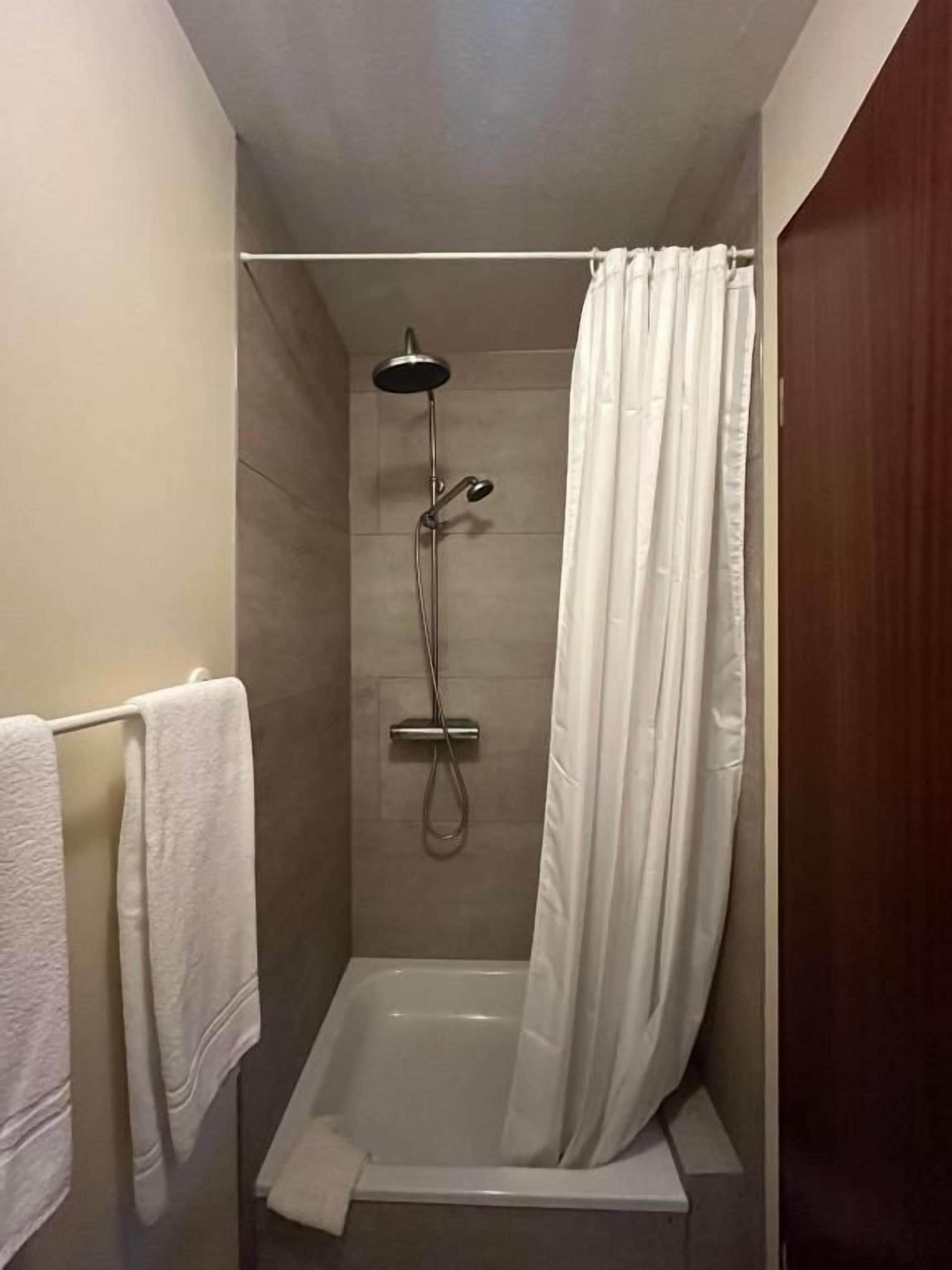 A shower area with a showerhead, curtain, and a towel rack with towels.