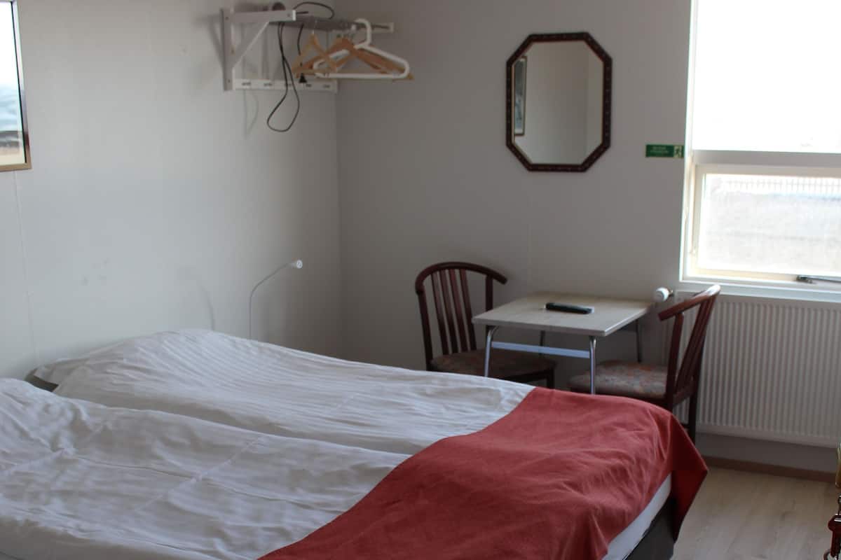 Un dormitorio con cama, escritorio y silla. Se ve un ventanal con vistas al exterior.