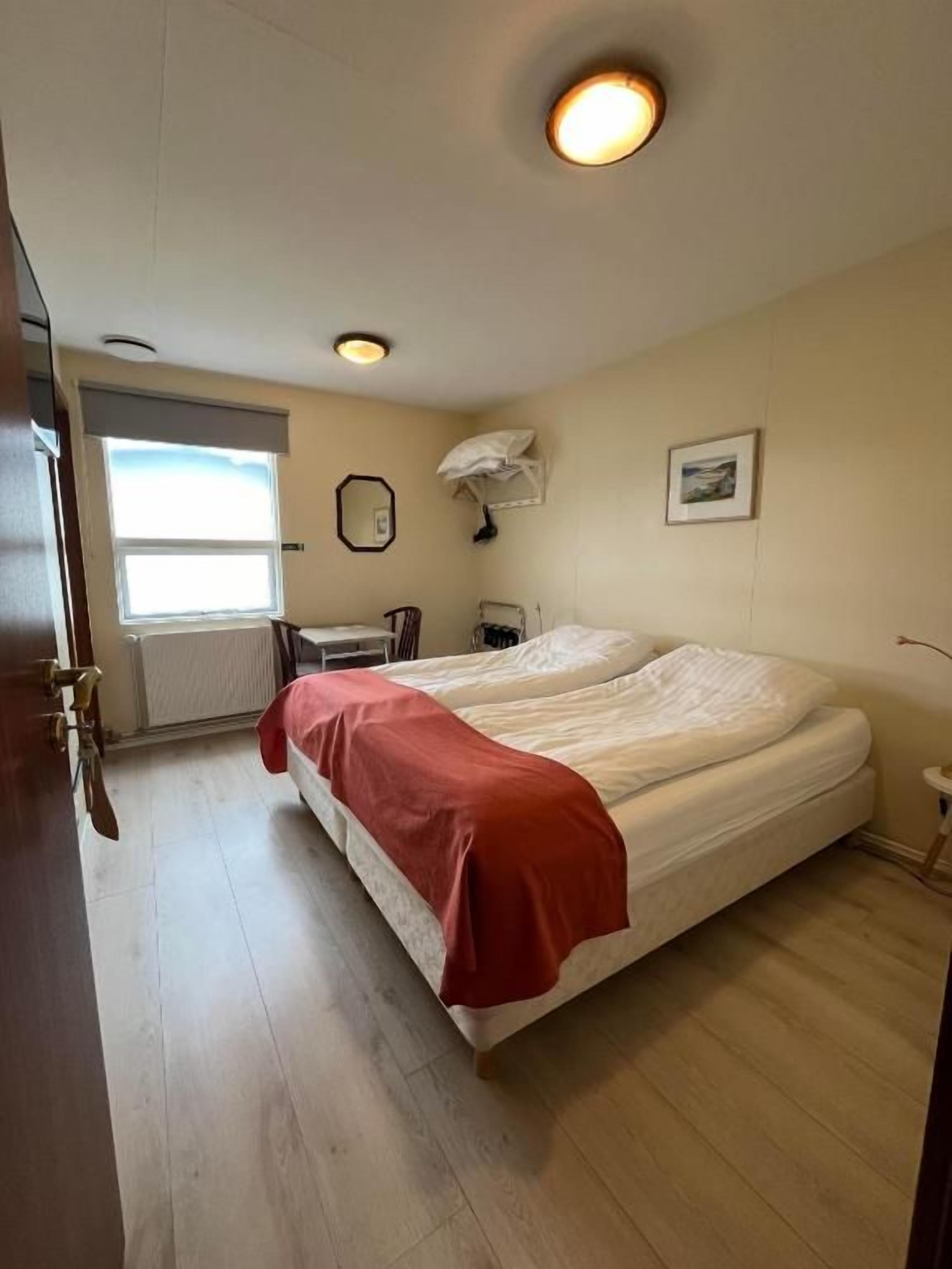 Una habitación de hotel con una cama, un ventanal, un radiador y una puerta.