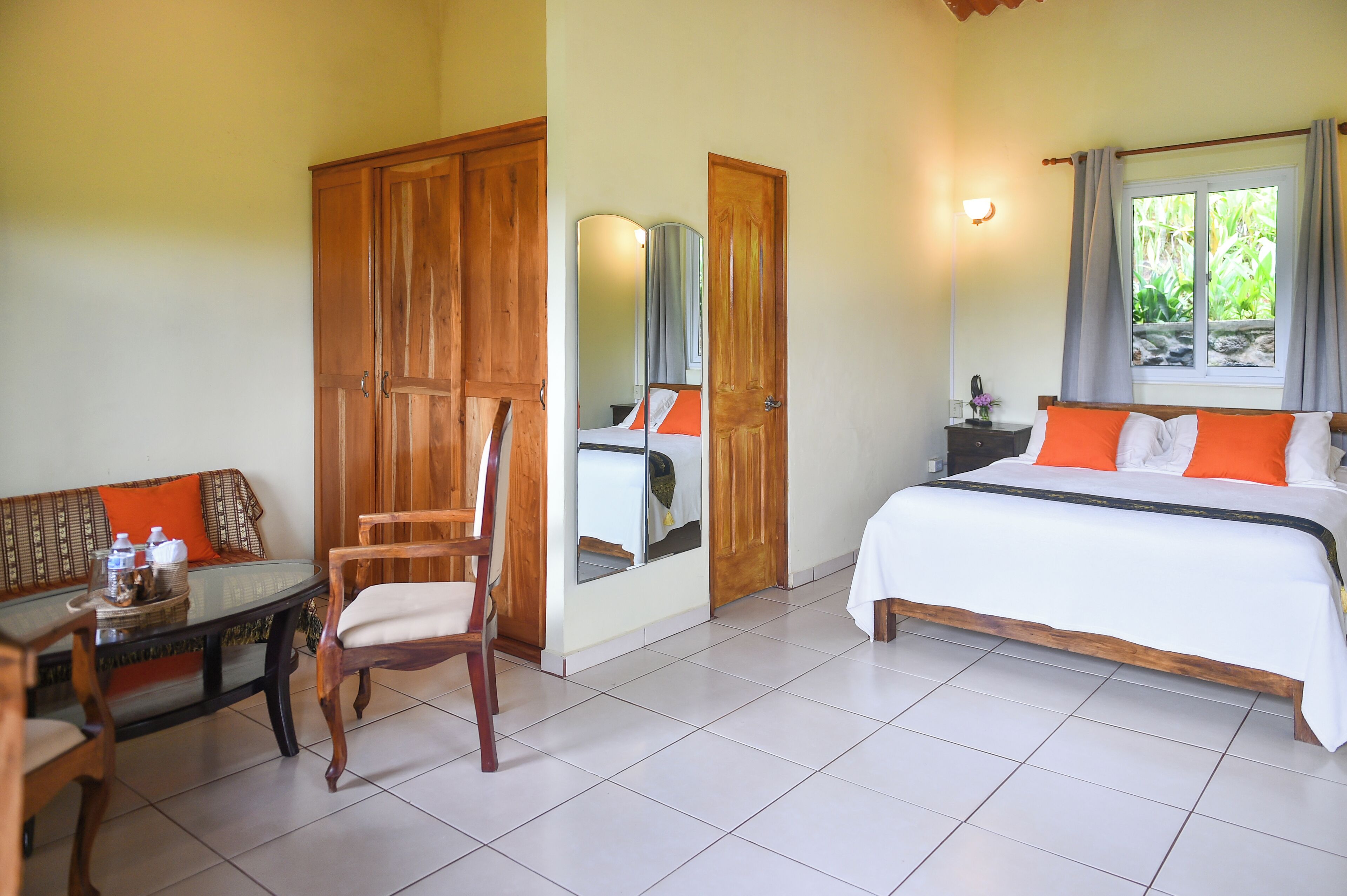 A hotel room with a bed, a sofa, a dining table, and a mirror.