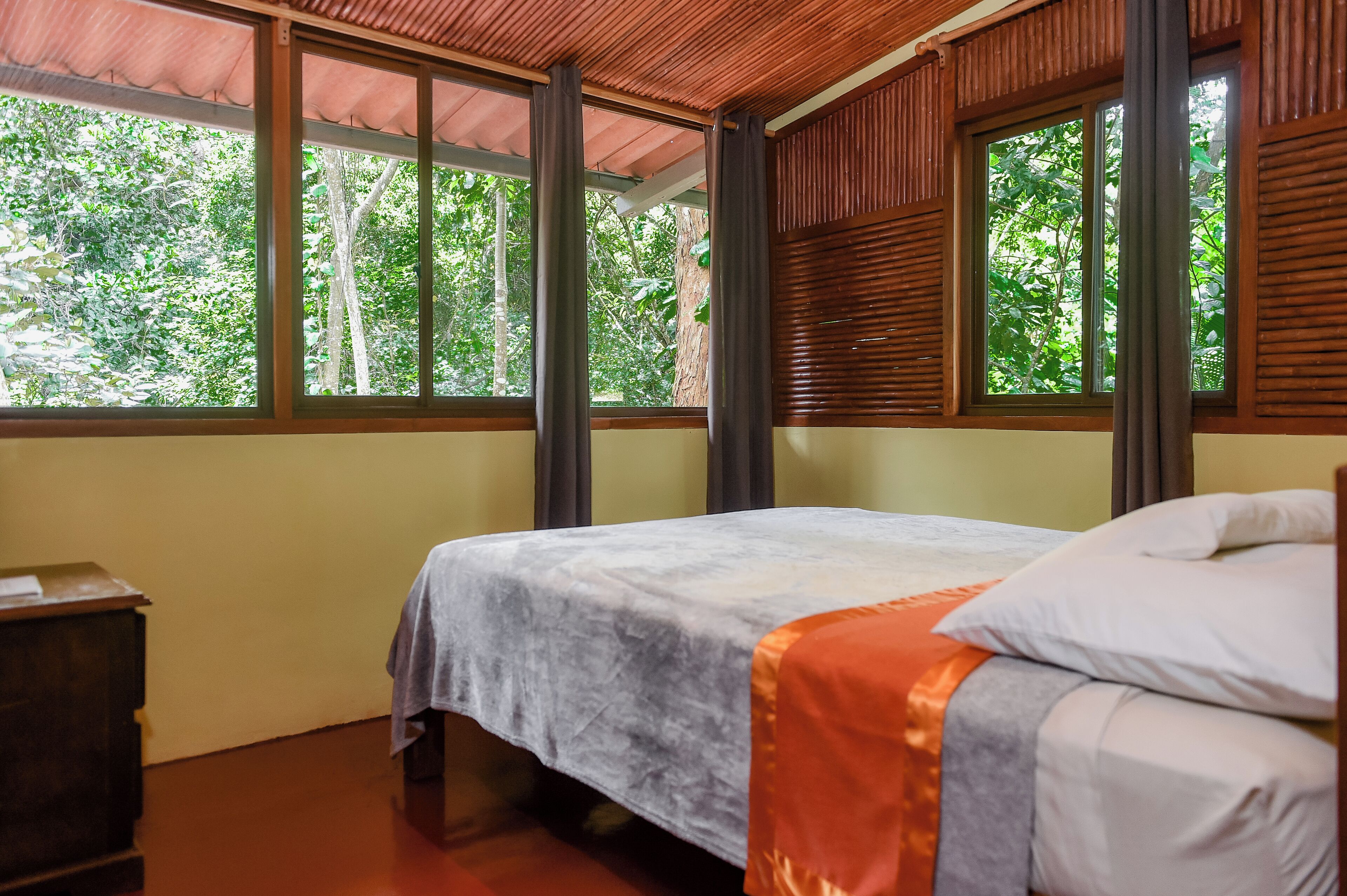 A room with a bed, a desk, and large windows with wooden shutters.