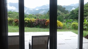 A view through a glass door of a patio area with a table and chairs, overlooking a lush garden and distant mountains. - Hotel Anachoreo (Santa Fe)
