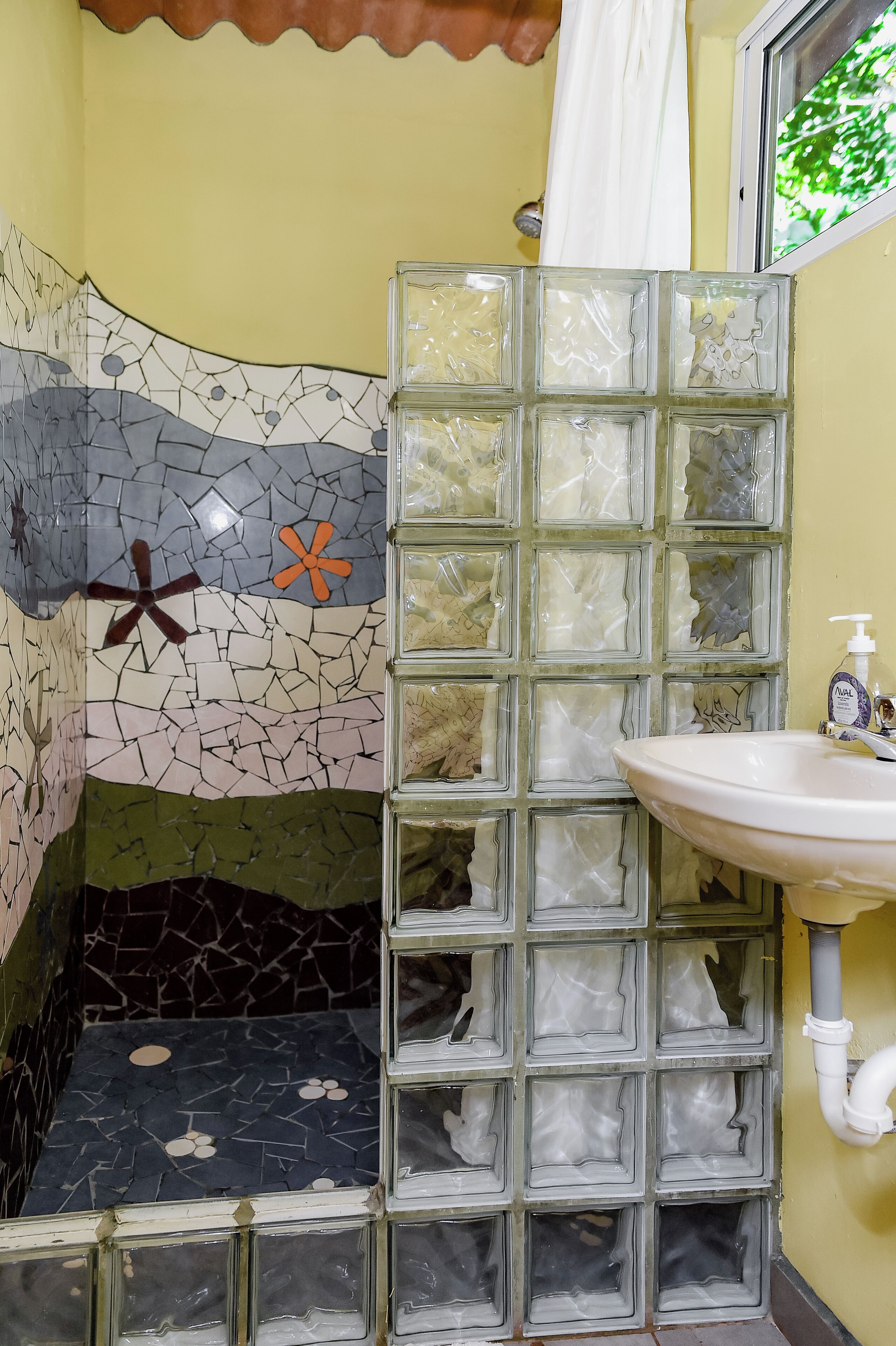 Ein Badezimmer mit Mosaikwand, einer Glasdusche und einem Waschbecken mit Seifenspender.