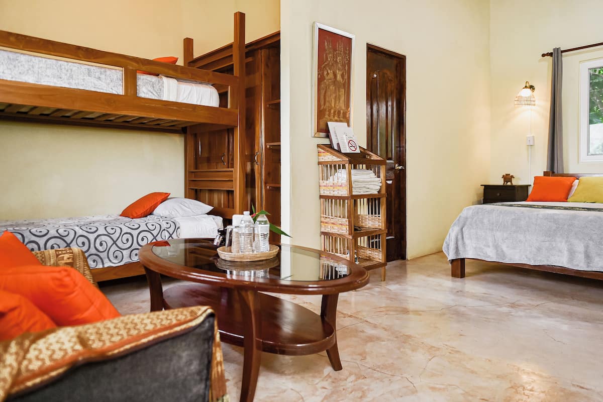 Habitación de hotel con dos camas individuales, una litera de madera, una mesita redonda con bandeja y una estantería.