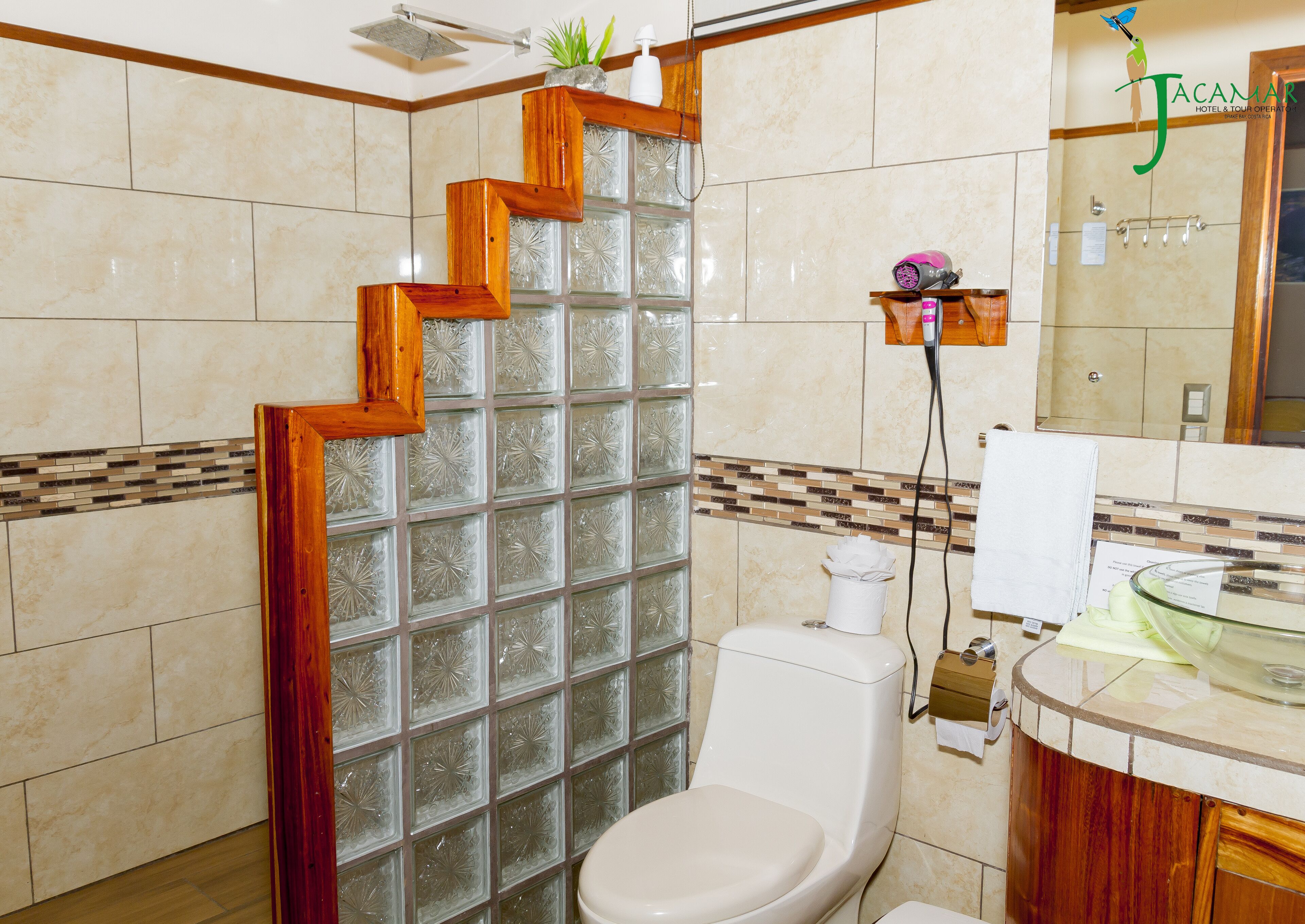 Un baño con cabina de ducha de vidrio, inodoro, tocador con espejo y escalera de madera.