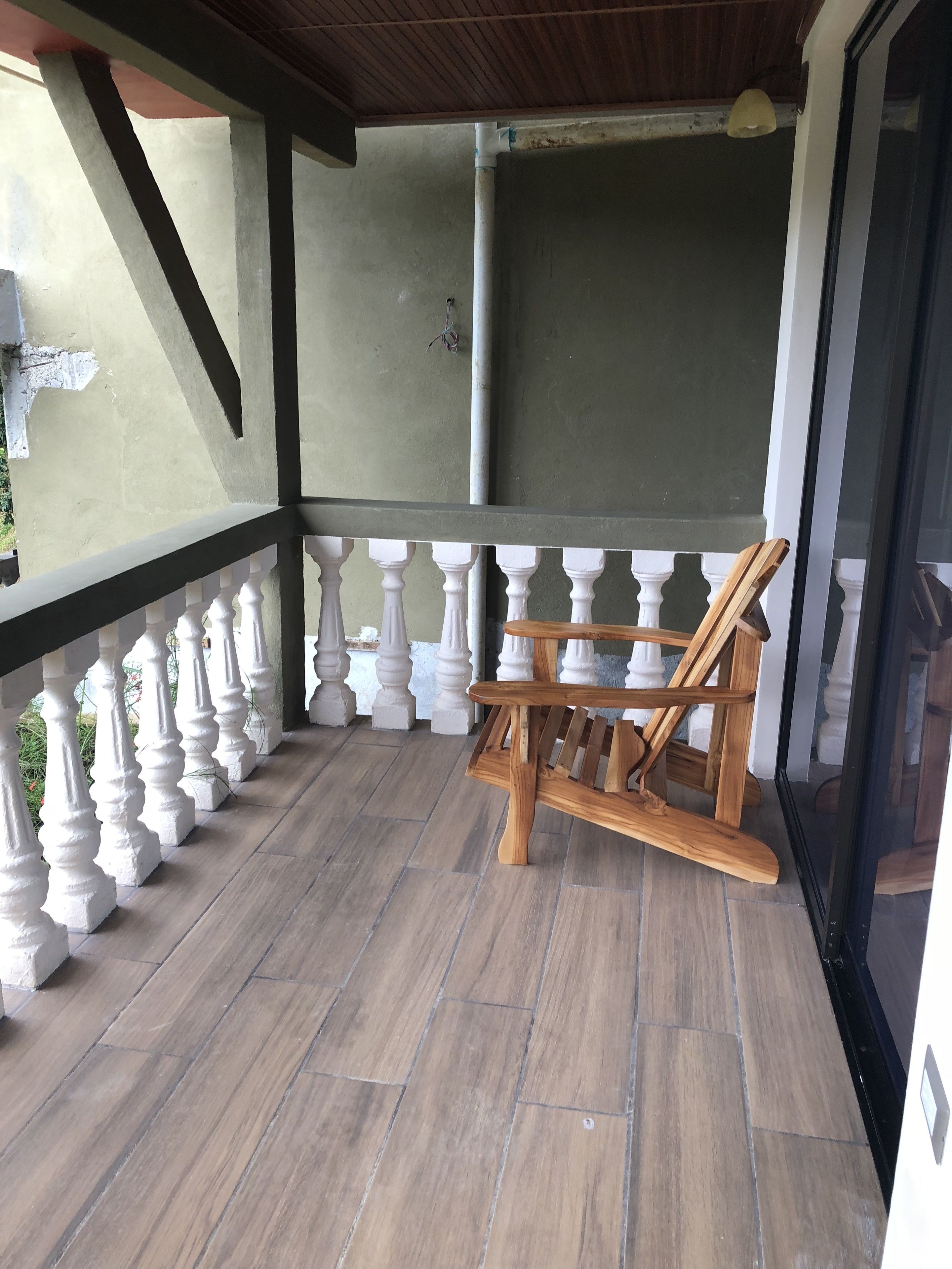 A wooden rocking chair on a tiled balcony with white balustrades.