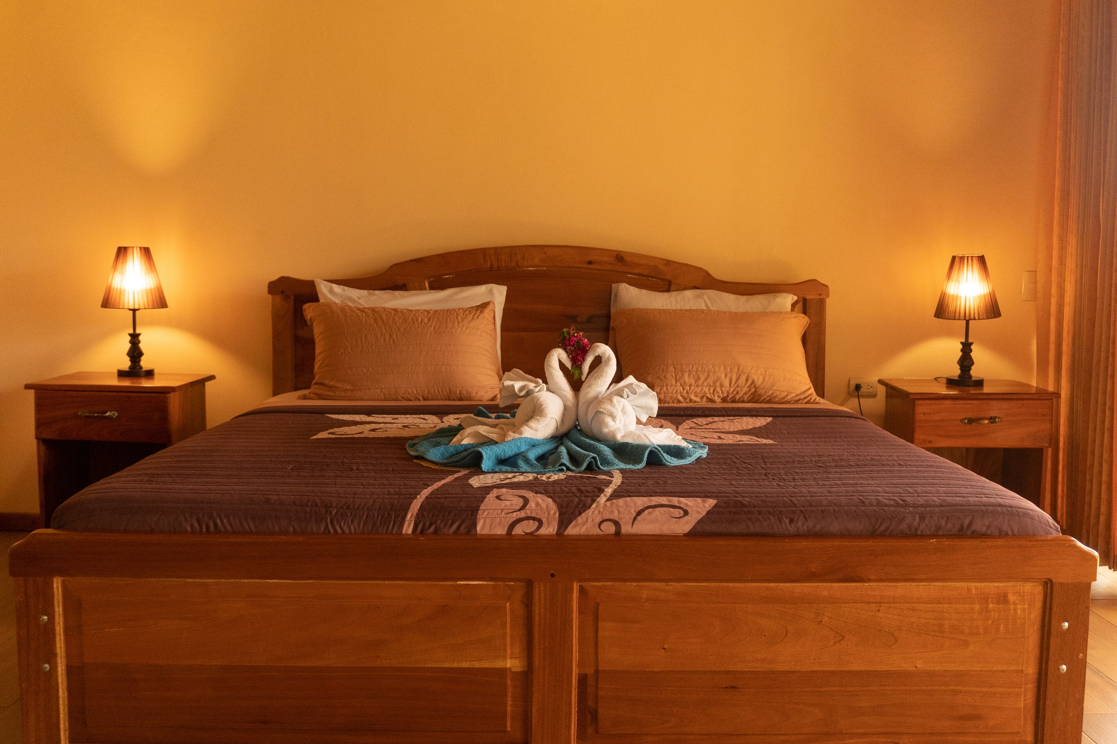 A neatly made bed with a wooden headboard, two bedside tables with lamps, and a decorative towel arrangement on the bed.