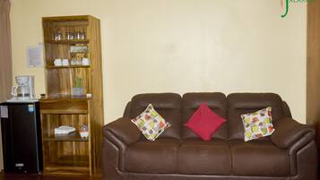 A brown leather sofa with two patterned cushions and a red pillow, a wooden cabinet with glassware, and a coffee maker on a small table.