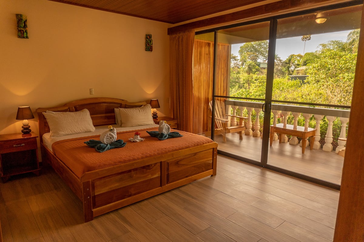 A wooden bed with a balcony, wooden nightstands, and a view of greenery.