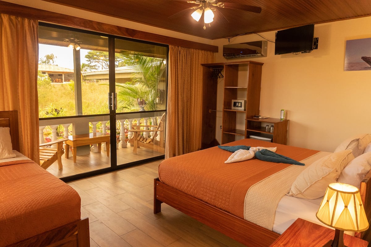 A hotel room with a large bed, a TV, a desk, and a balcony with outdoor furniture.