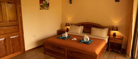 A bedroom with a wooden bed, two bedside tables with lamps, a wooden wardrobe, and two wall-mounted paintings.