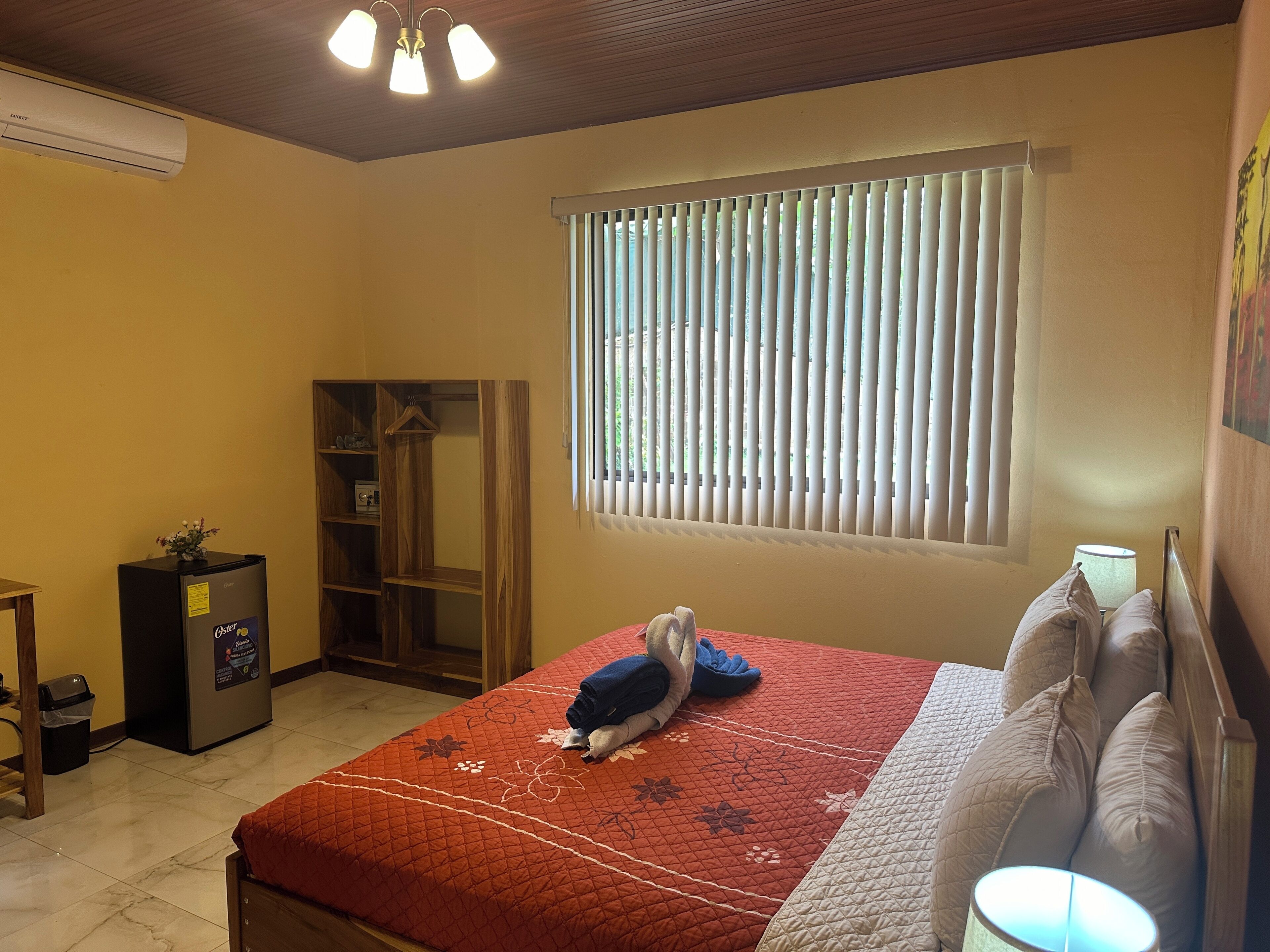 A bedroom with a bed, a wardrobe, a small table, and a window with blinds.
