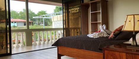 A bedroom with a large sliding glass door leading to a balcony, a wooden bed, a nightstand, and a built-in shelving unit.
