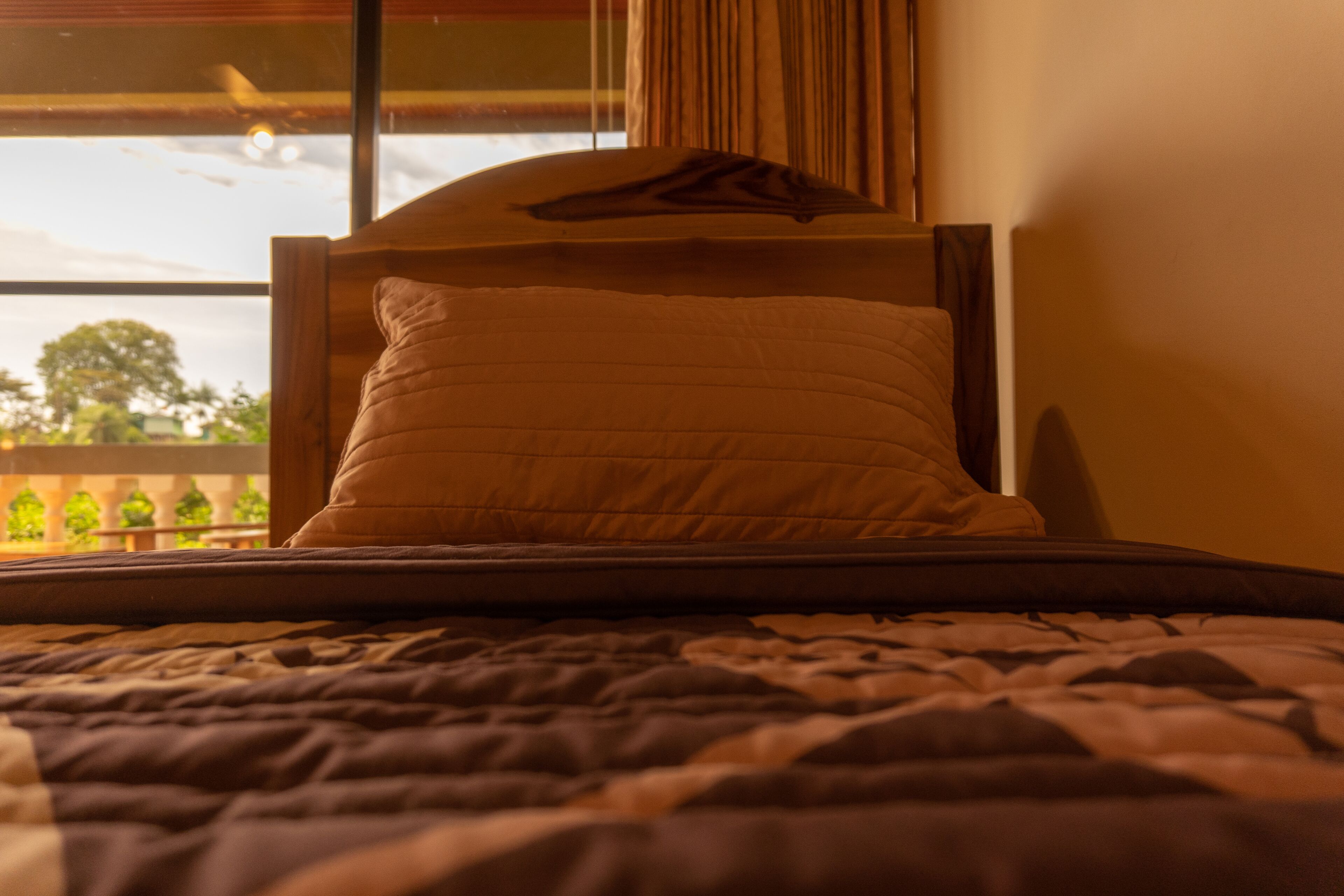 Una cama con cabecera, una ventana con cortinas y vistas al verdor exterior.
