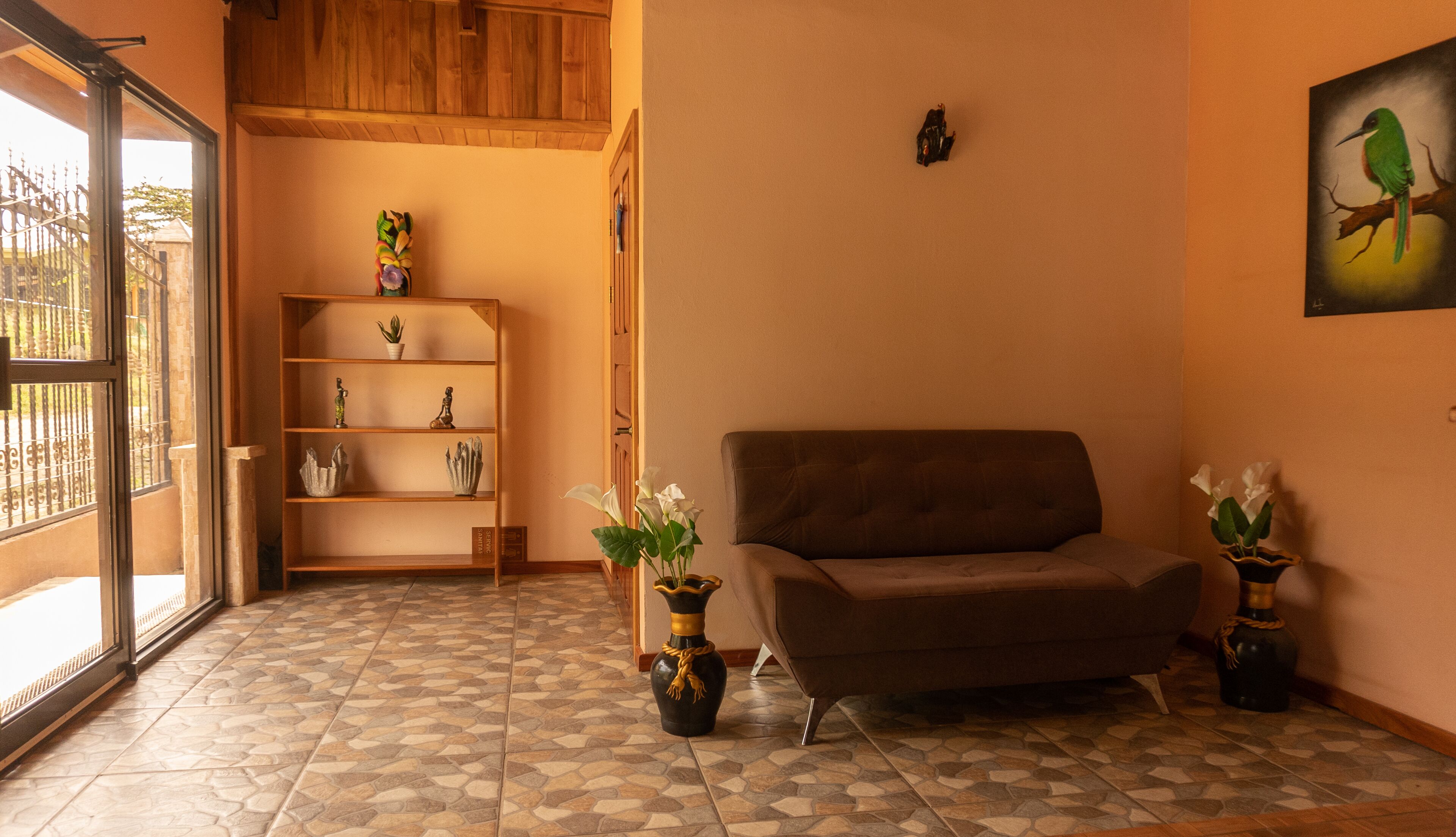 A living room with a brown sofa, a wooden bookshelf, and two vases with flowers.