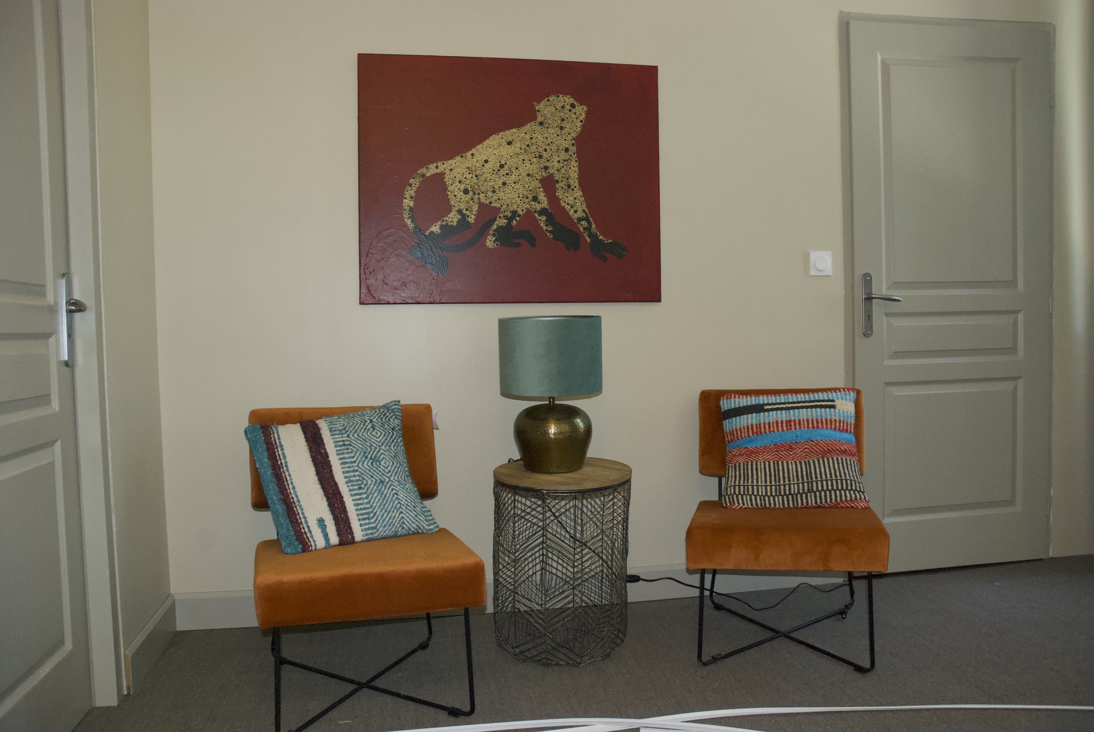 A hallway with two orange chairs, a patterned pillow on each, a lamp, and a leopard painting on the wall.