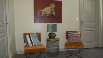A hallway with two orange chairs, a patterned pillow on each, a lamp, and a leopard painting on the wall.
