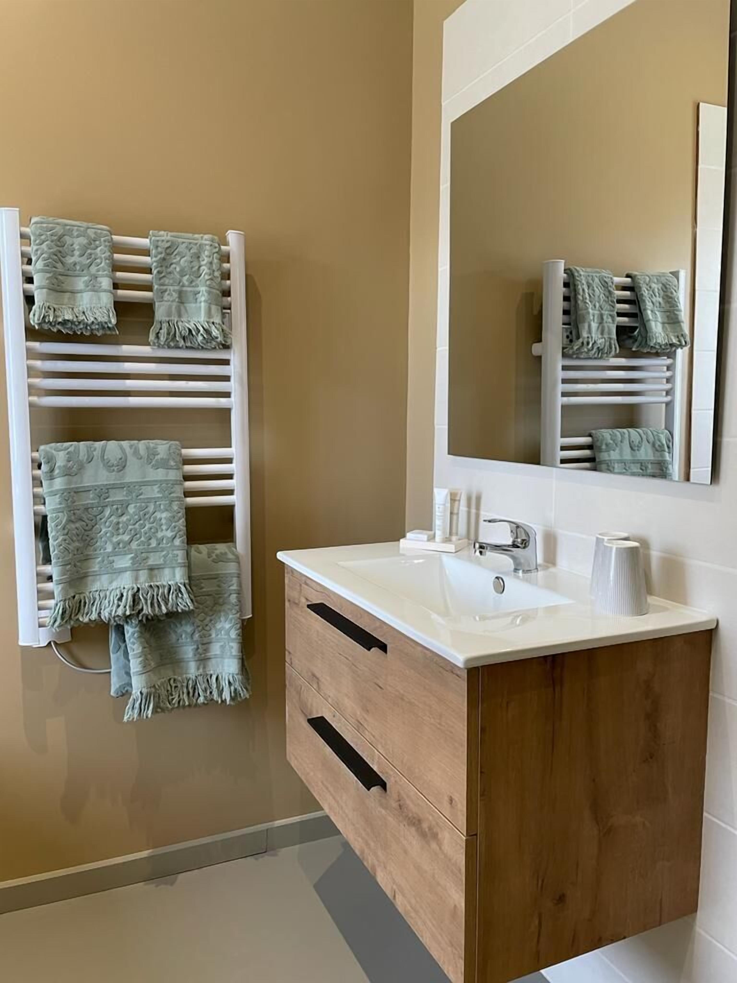 A bathroom with a white sink, wooden cabinet, and a towel rack with green towels.