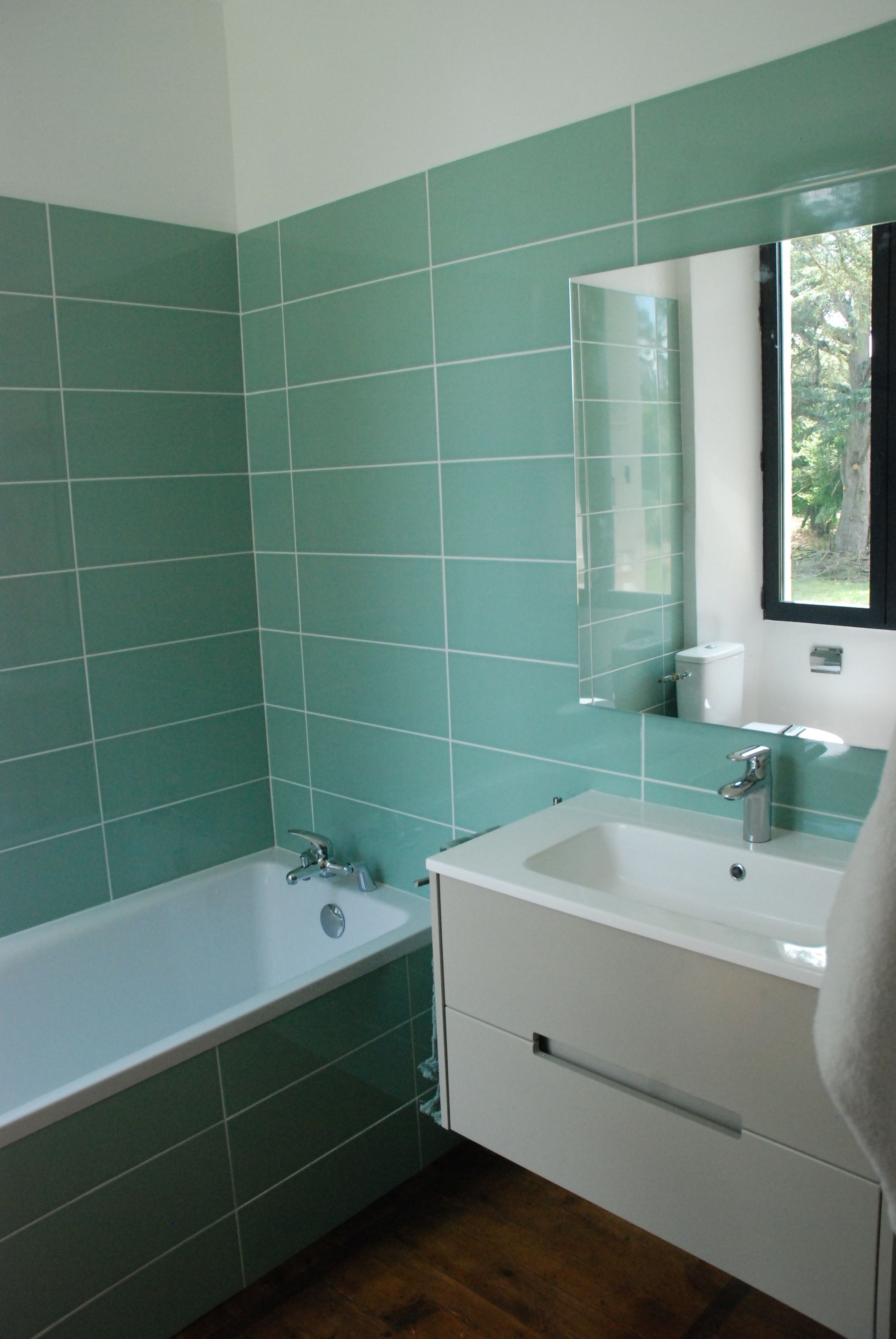Un baño con baldosas verde mar, un lavamanos blanco y una bañera.