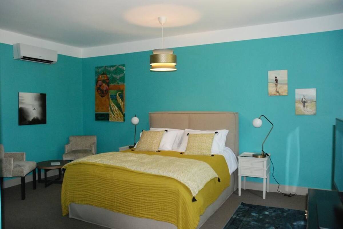 A bedroom with a bed, two bedside tables, a chair, and artwork on the walls.