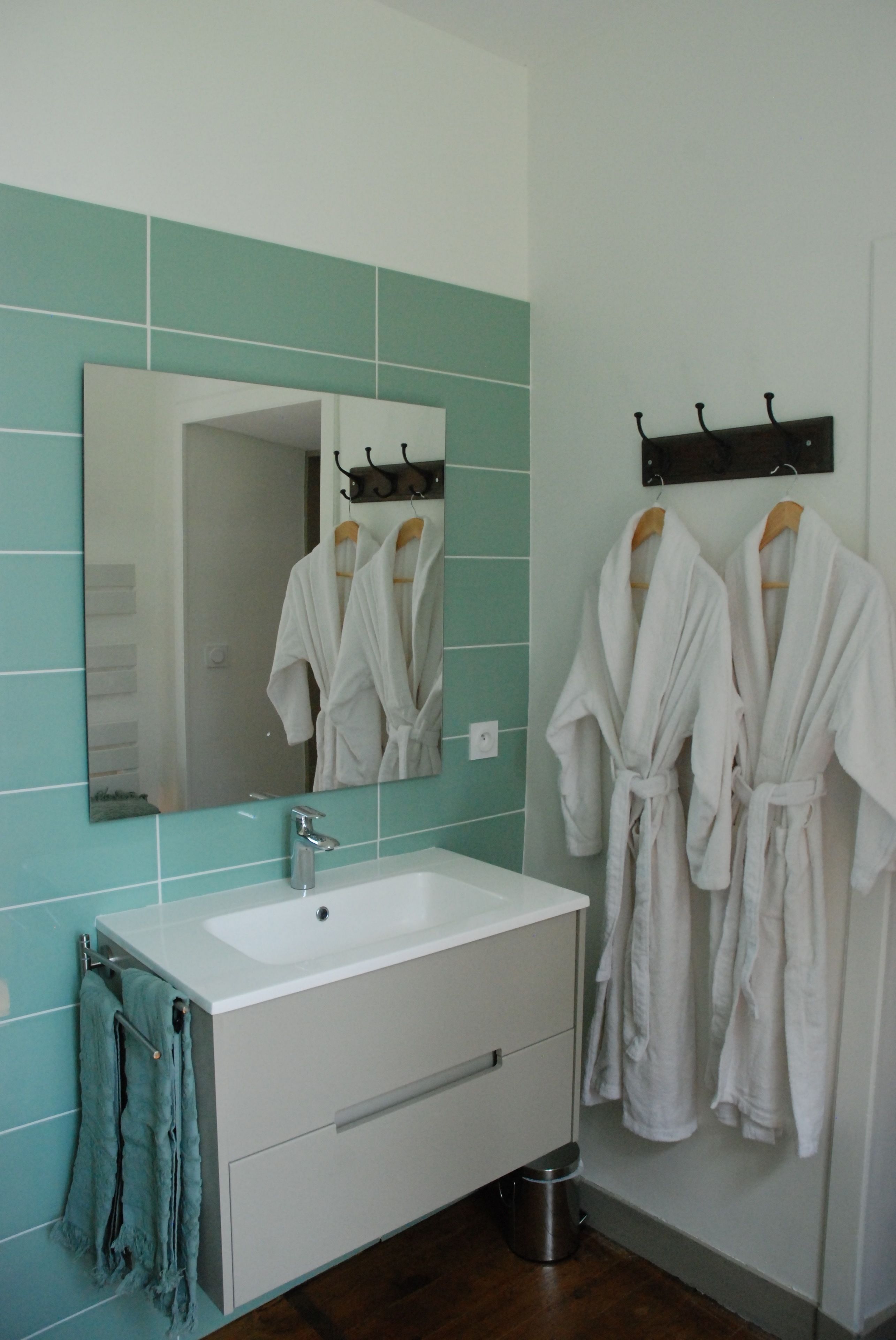 A bathroom with a white sink, a mirror, and two white robes hanging on hooks.