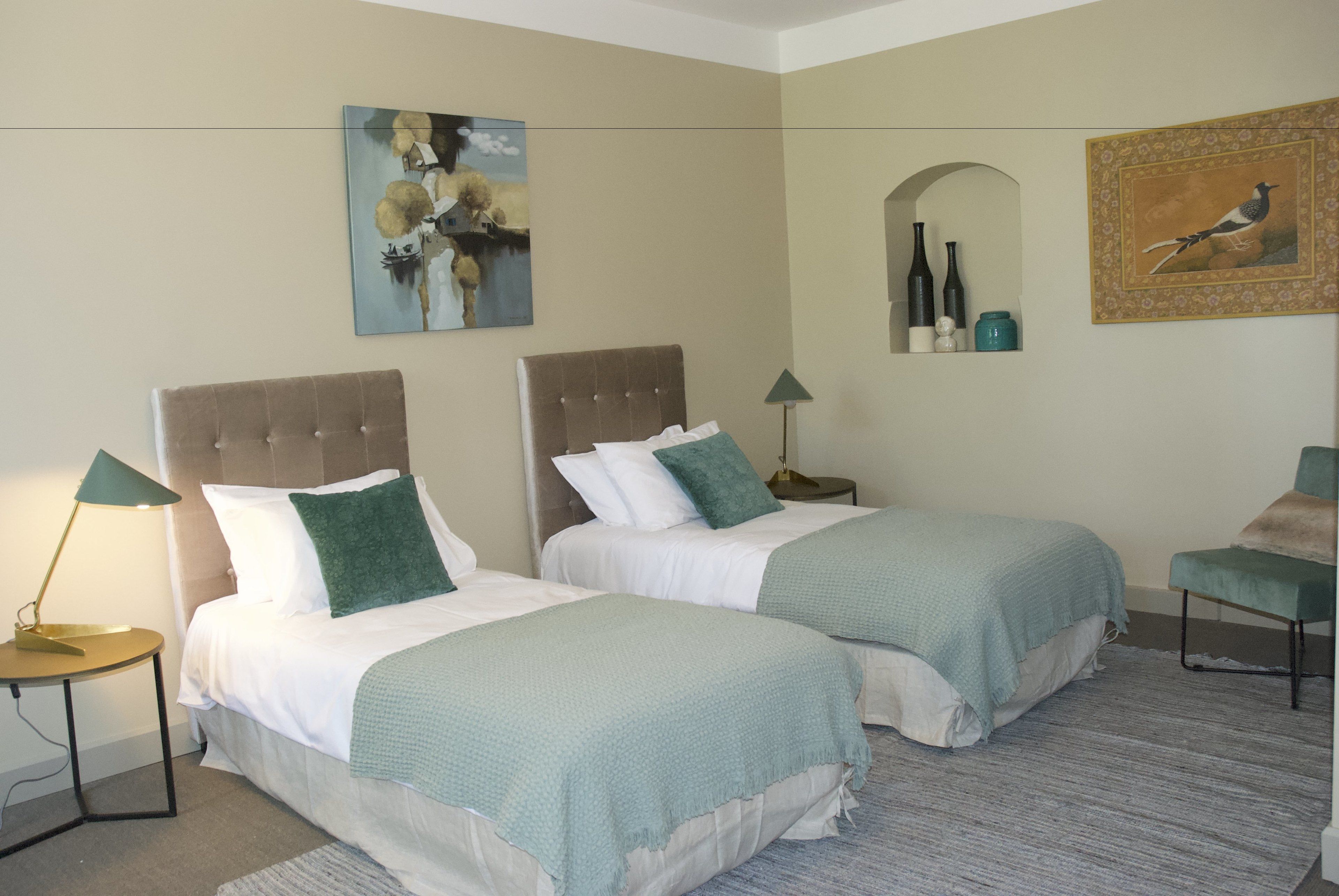 A hotel room with two beds, a small table, a lamp, and artwork on the walls.