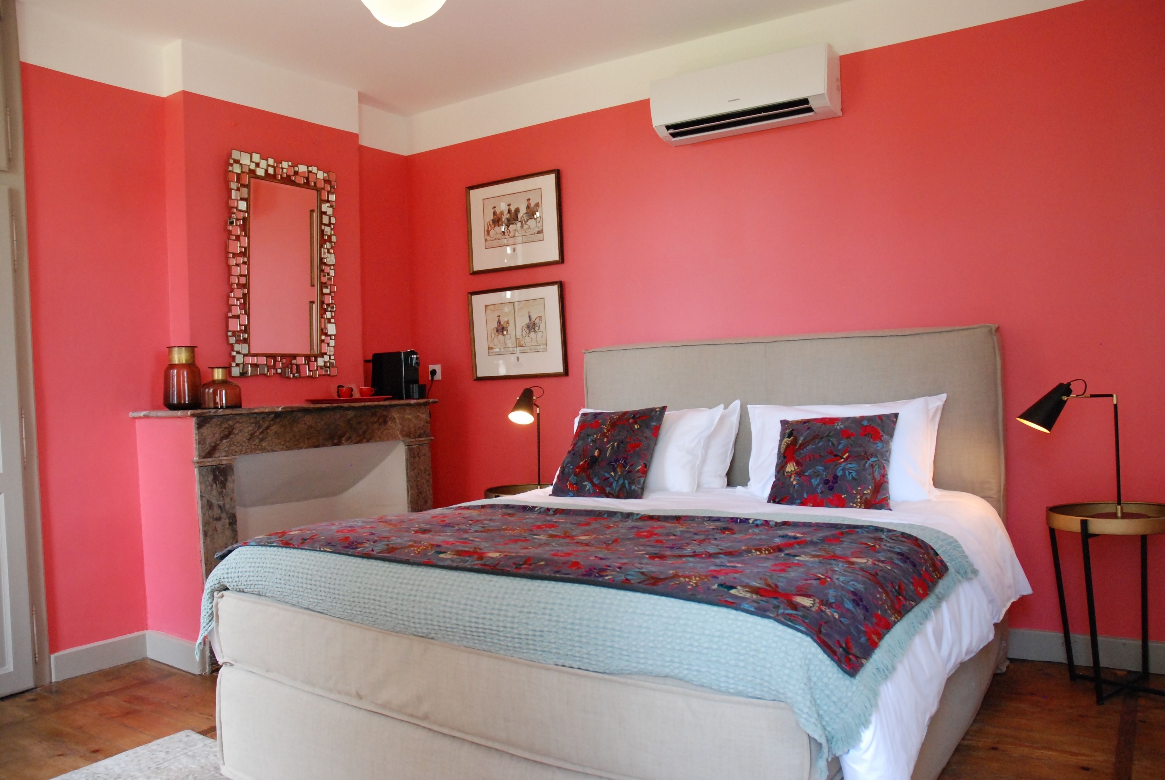 Une chambre à coucher comprenant un lit, un miroir, deux tableaux encadrés, une lampe de chevet et un climatiseur.
