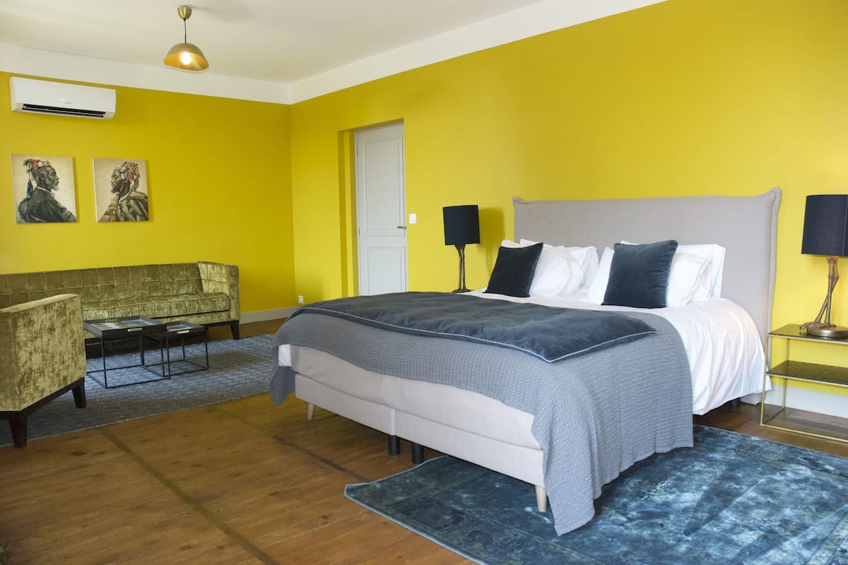 A bedroom with a bed, bedside tables, a sofa, and artwork on the walls.