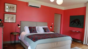A bedroom with a bed, two bedside tables, a nightstand, a wall-mounted air conditioner, and a ceiling light fixture.