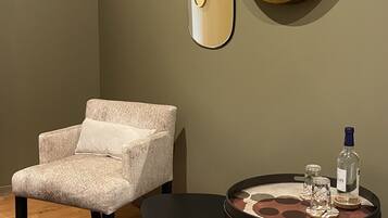 A room with a herringbone-patterned armchair, a round mirror, a small round table with a tray, and a patterned rug.