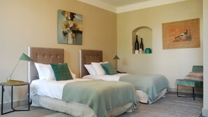 A hotel room with two beds, a green chair, a small table, and artwork on the walls.