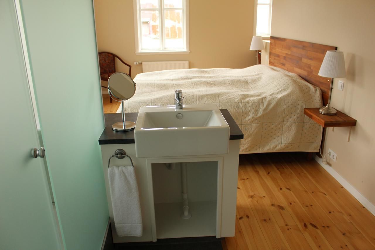 Een slaapkamer met een houten bed, een nachtkastje met een lamp, een klein nachtkastje spiegel, en een witte wastafel met een handdoek erover.