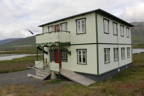 Un edificio de dos pisos con un balcón, una puerta roja y una bandera.