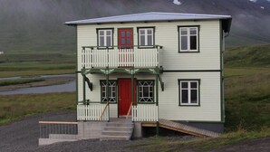 A two-story building with a red door, a balcony, and a small ramp leading to the entrance.