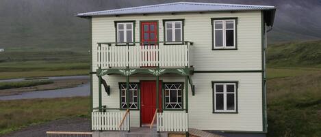 A two-story building with a red door, a balcony, and a small ramp leading to the entrance.