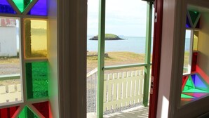 A view from a room with colorful stained glass windows overlooking a grassy area and a small island in the distance.
