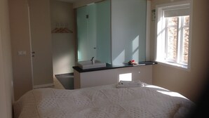 A bedroom with a bed, a bedside table, a mirror, and a window.