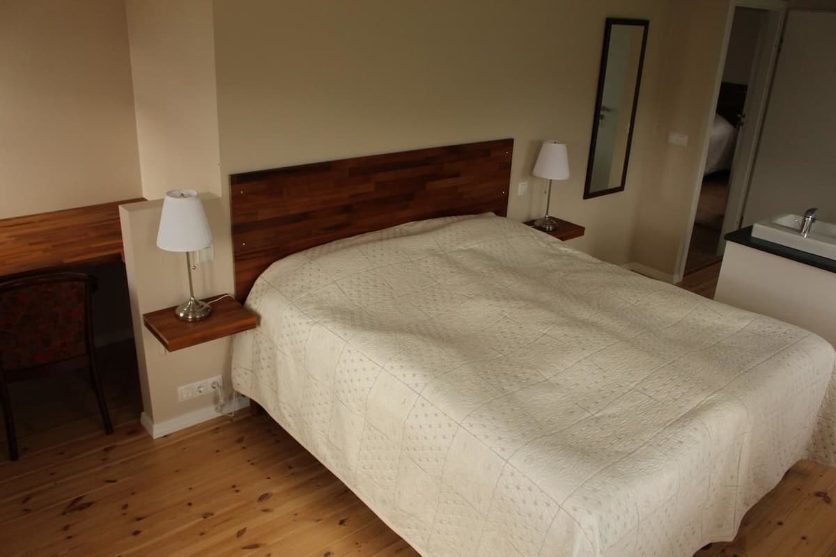 Habitación de hotel con cabecera de madera, cama con colcha acolchada, lámparas de noche, una mesita y un espejo.