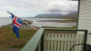 A balcony with a flag, a chair, and a view of a lake and mountains.