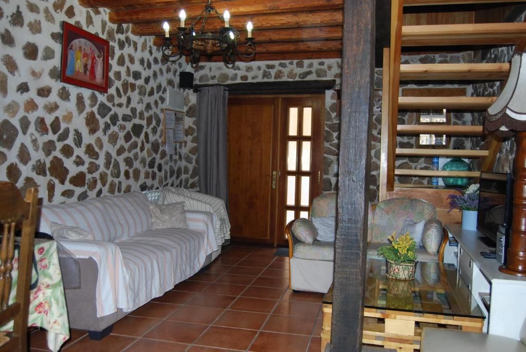 Una habitación con pared de piedra, puerta de madera, un sofá, una silla y una mesa con una planta.