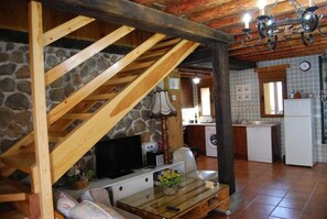 Una cocina rústica con pared de piedra, vigas de madera, un lavabo y una lavadora.