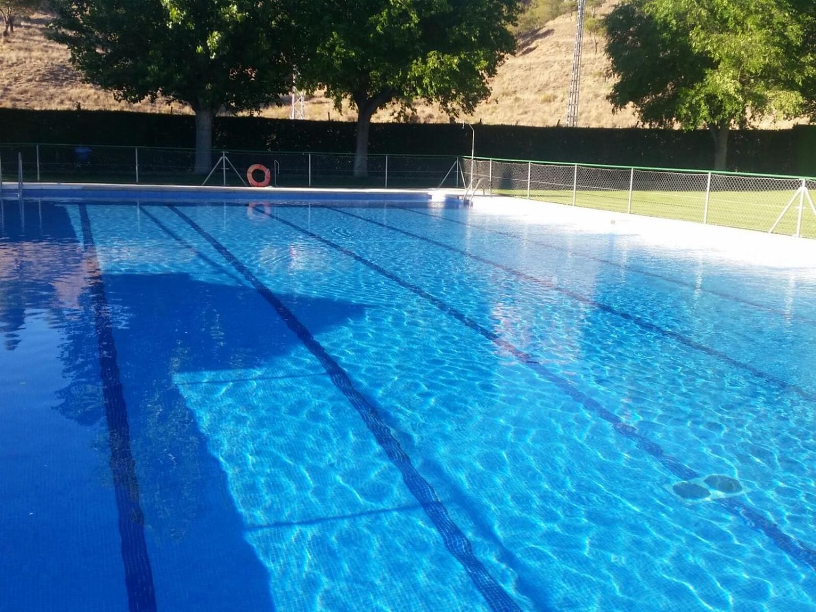 Una piscina blava i nítida amb separadors de carrils, envoltada per una tanca i arbres.
