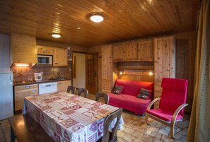 A wooden interior with a dining table, chairs, a red sofa, and a kitchen area. - La Fleche D'or (Chatel)