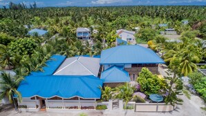 Ein Resort mit mehreren Gebäuden, darunter ein großes mit blauem Dach, umgeben von üppigen Palmen und viel Grün.